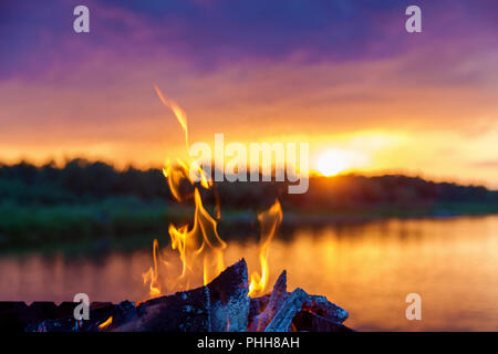 Red lingue di fiamma dal fuoco nei pressi del fiume al tramonto. Foto Stock