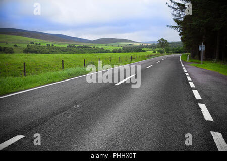Strada asfaltata attraverso il campo verde e nubi sul cielo blu Foto Stock