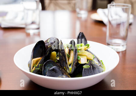 Le cozze in gusci in una ciotola bianca con una salsa verde su un tavolo da pranzo. Foto Stock