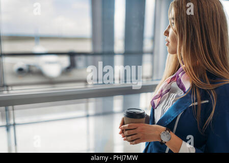 Hostess con caffè e la valigia seduto sul sedile nella zona di attesa in aeroporto. Hostess con il bagaglio e assistente di volo con il bagaglio a mano, aviatran Foto Stock