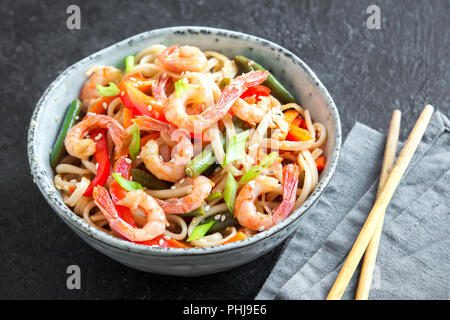 Stir fry con udon noodles, gamberi (gamberetti) e verdure. Asian cibo sano, pasto, friggere in un recipiente su sfondo nero, copia dello spazio. Foto Stock