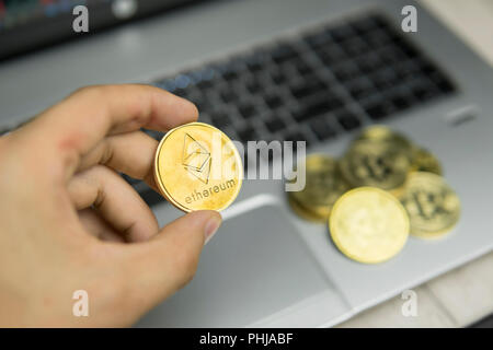 Imprenditore maschio mano azienda Ethereum moneta su uno sfondo di tastiera portatile e la pila di monete d'oro. Denaro virtuale e la crescita finanziaria concetto. Trading di Data Mining Ethereum Foto Stock
