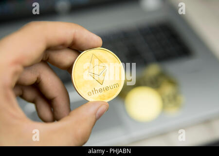 Imprenditore maschio mano azienda Ethereum moneta su uno sfondo di tastiera portatile e la pila di monete d'oro. Denaro virtuale e la crescita finanziaria concetto. Trading di Data Mining Ethereum Foto Stock