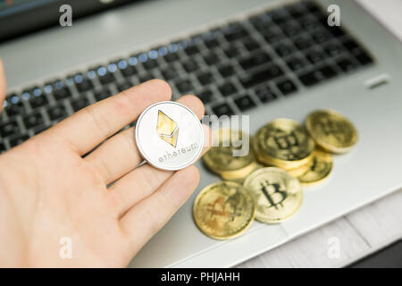 Imprenditore maschio mano azienda Ethereum moneta su uno sfondo di tastiera portatile e la pila di monete d'oro. Denaro virtuale e la crescita finanziaria concetto. Trading di Data Mining Ethereum Foto Stock