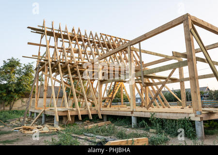Le travi di legno di una nuova casa in costruzione al tramonto. Casa di nuova costruzione con interni esposti framing. Foto Stock