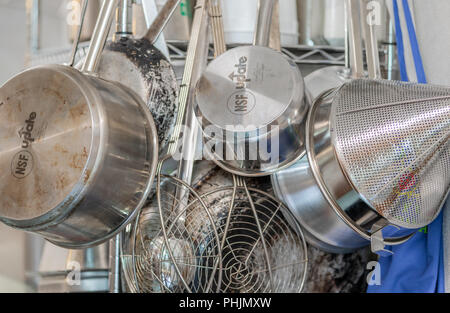 Un gruppo di acciaio inossidabile pentole, padelle e di filtri appesi in una cucina commerciale Foto Stock