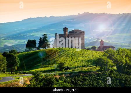 Vista sul castello di Grinzane Cavour al tramonto, il cielo è giallo e arancione e alcuni raggi solari illuminano la Manor in controluce Foto Stock