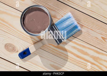 Sbollentati tavole di pino pronto per la verniciatura nel colore marrone, una spazzola con setole blu e una latta di vernice sulla superficie, la spazzola si trova accanto al bicchiere Foto Stock