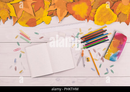 Notebook vuota e forniture scolastiche sul tavolo in legno con foglie dipinte. Foto Stock