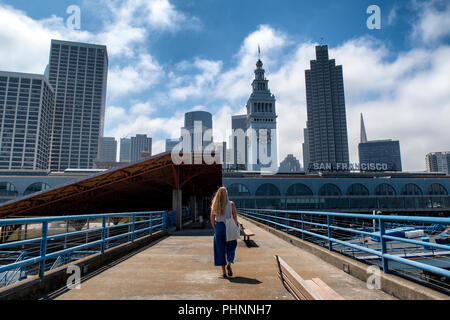 Una donna cammina lungo un molo verso il ferry building a San Francisco, California. Foto Stock