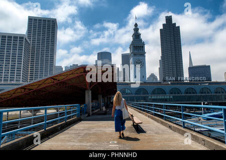 Una donna cammina lungo un molo verso il ferry building a San Francisco, California. Foto Stock