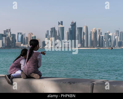 Due Arabian medio Pasqua Bambino ragazze seduti sulla Corniche Broadway e guardando a Doha dello Skyline. Il Qatar, Medio Oriente Foto Stock