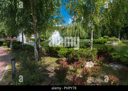 Il pittoresco parco con laghetto ornamentale con fontane circondate da foglia verde di ombrosi alberi e rocce Foto Stock