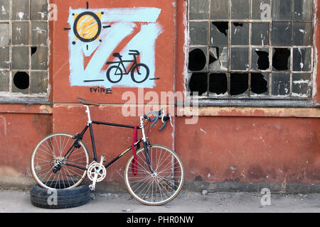 Stile tradizionale bicicletta di fronte abbandonato coperto di graffiti edificio in fabbrica con le finestre rotte Foto Stock