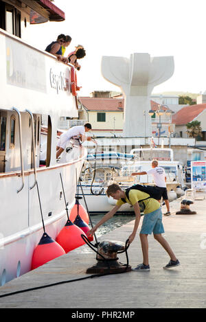 Vodice Croazia - Agosto 11, 2018: una nave da crociera di Carpe Diem arrivando a Vodice e docking. Un uomo e un ragazzo adolescente su un molo il fissaggio della corda di nave Foto Stock