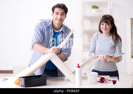 Moglie aiutando il marito per riparare sedia rotta a casa Foto Stock