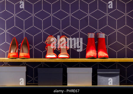 Scarpe rosso sul ripiano in negozio con sfondo scuro e alcune scatole Foto Stock