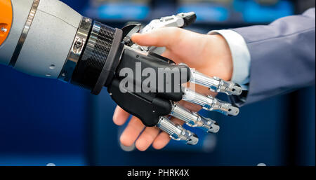 La mano di un uomo d'affari che stringono le mani con un droid robot. Il concetto di interazione umana con intelligenza artificiale. Foto Stock