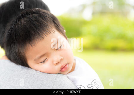 Closeup ritratto di carino bambina di dormire sulla spalla delle madri in giardino sfondo, felice giovane famiglia amorevole, nuovo concetto di vita. Foto Stock