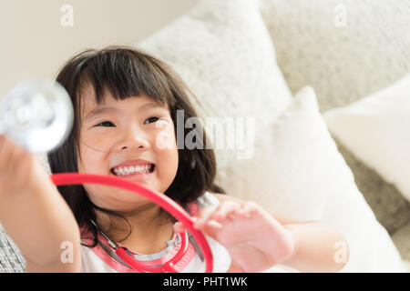 Carino bambina è sorridente e riproduzione medico con stetoscopio e orso di peluche. Kid e health care concetto. Foto Stock