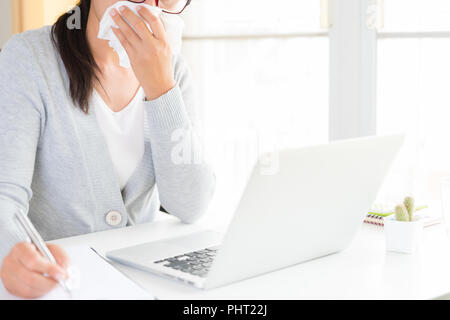 Young business woman malati in ufficio, mano azienda s tessuto e neezing in un tessuto bianco. portatile sul tavolo. Sanità e medicina concetto. Foto Stock