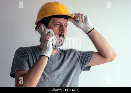 Tecnico delle Costruzioni parlando al telefono cellulare, gravi maschio adulto persona utilizza lo smartphone per la comunicazione con i lavoratori sul sito di costruzione Foto Stock