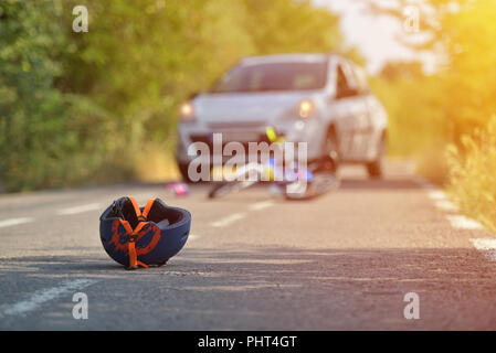 Close-up di un ciclismo casco caduto su asfalto accanto a una bicicletta dopo l incidente di auto sulla strada in città Foto Stock