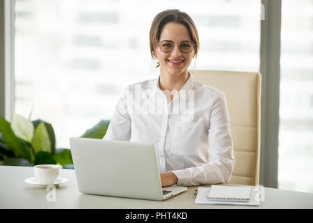 Sorridente imprenditrice millenario seduto alla scrivania con lapto Foto Stock