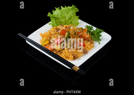 Mi Xao stir-fried noodles piatti asiatici sulla piastra triangolare isolati su nero. Servita con bacchette. Foto Stock