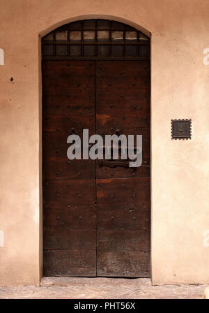 Il vecchio di legno marrone scuro e porta, con elementi in ferro battuto e la chiusura a scatto in una luce marrone parete in stucco Foto Stock