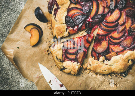 Flat-lay di prugna galetta torta dolce sulla carta da forno su cemento grigio Sfondo, vista dall'alto. Caduta stagionale o dessert autunnale Foto Stock