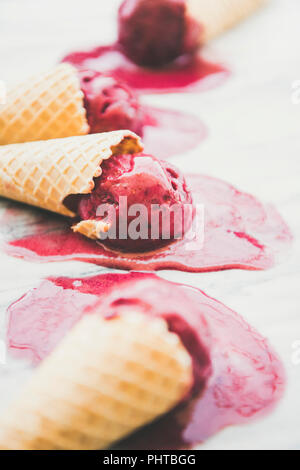 Freschi dessert estivo. La fusione naturale di lampone sorbetto gelato scoop in cialde dolci coni su sfondo marmo, il fuoco selettivo. Vegano sano s Foto Stock