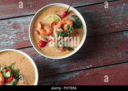 Tradizionale zuppa tailandese Tom Yum con gamberetti e funghi, serviti con un fresco e fettine di lime. Vista superiore e rustico sfondo di legno Foto Stock