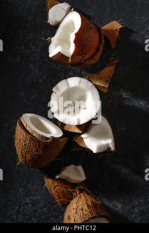 Chiudere l immagine di noci di cocco incrinato disposti sulla trama scuro dello sfondo. Hard Light. Foto Stock
