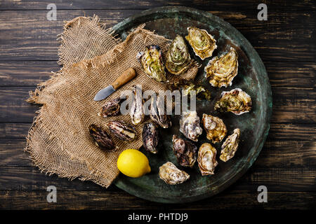 Un assortimento di ostriche fresche, coltello e limone nel vassoio su sfondo scuro Foto Stock