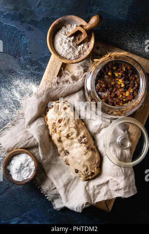 Torta di Natale, tradizionale festa tedesca la cottura. Pasta integrali lo Stollen di preparazione sul tovagliolo di lino con ciotole di farina e uva passa oltre il blu scuro Foto Stock