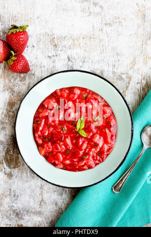 Fragole Confettura di basilico servito in una ciotola di smalto. Fotografato su un rustico sfondo bianco. Foto Stock