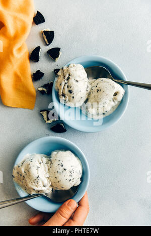 Donna che mantiene un vaso di biscotti al cioccolato gelato fotografata da vista dall'alto. Un altro vaso di gelato e biancheria di colore giallo accompagnare. Foto Stock