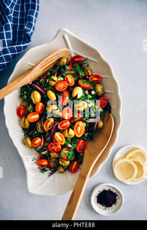 Insalata di olive verdi schiacciate con erbe aromatiche, cipolla, insaporito con limone, olio d'oliva e melograno melassa servita con due cucchiai di legno in un bianco insalatiera con Foto Stock