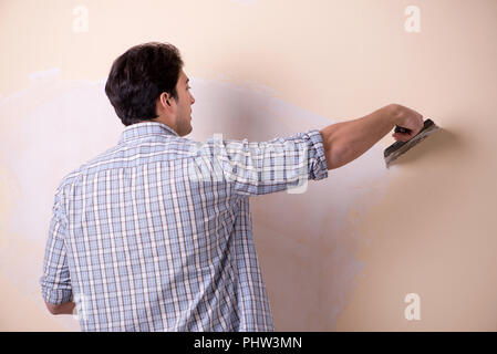 Giovane uomo applicando intonaco sulla parete di casa Foto Stock