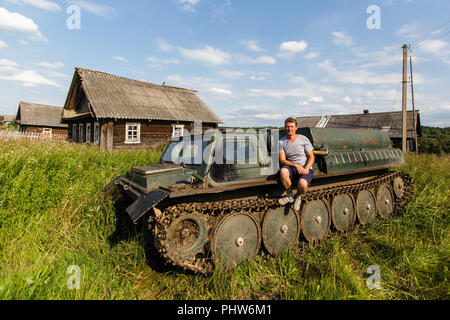 Un uomo si siede sulla corazza di vecchio veicolo fuoristrada in russo il villaggio. Foto Stock