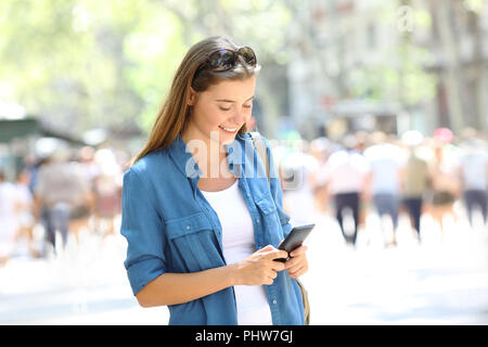 Donna felice utilizza una smart phone in piedi in strada Foto Stock