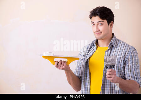 Giovane uomo applicando intonaco sulla parete di casa Foto Stock