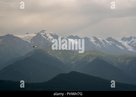 Un vecchio stile sovietico elicottero vola attraverso un paesaggio impressionante vista di Snow capped Caucaso gamme della montagna. Foto Stock