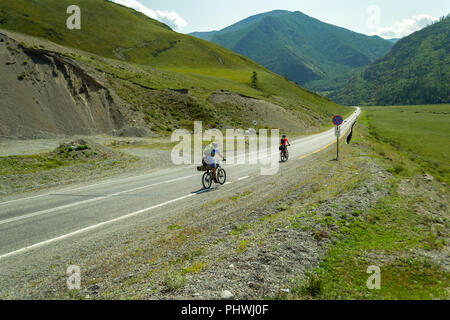 Un paio di uomo e donna nei caschi ride su sport biciclette su una strada nelle montagne di Altai salendo Foto Stock