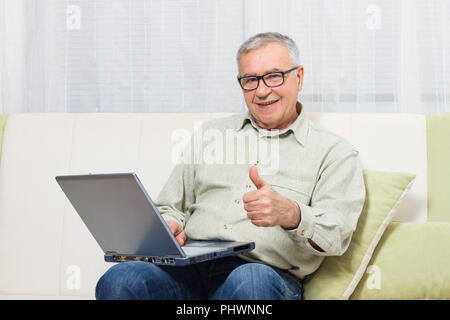 L'uomo anziano che mostra il pollice mentre si utilizza il laptop. Foto Stock