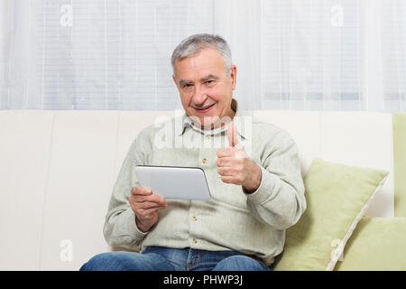 L'uomo anziano che mostra il pollice mentre si utilizza digitale compressa. Foto Stock