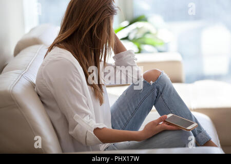Triste donna seduta sul divano tenendo il telefono in attesa di chiamata Foto Stock