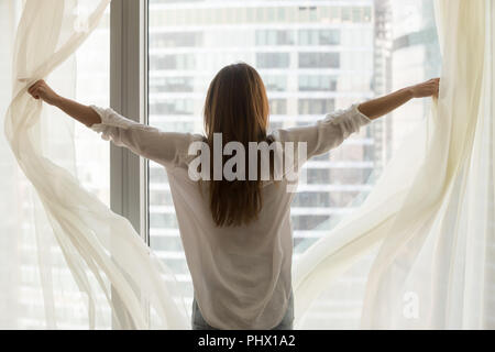 Vista posteriore a donna apertura di tende a vetro feeling free independ Foto Stock