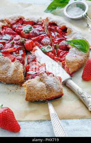 Tagliare la torta fatta in casa con fragole e basilico. Foto Stock